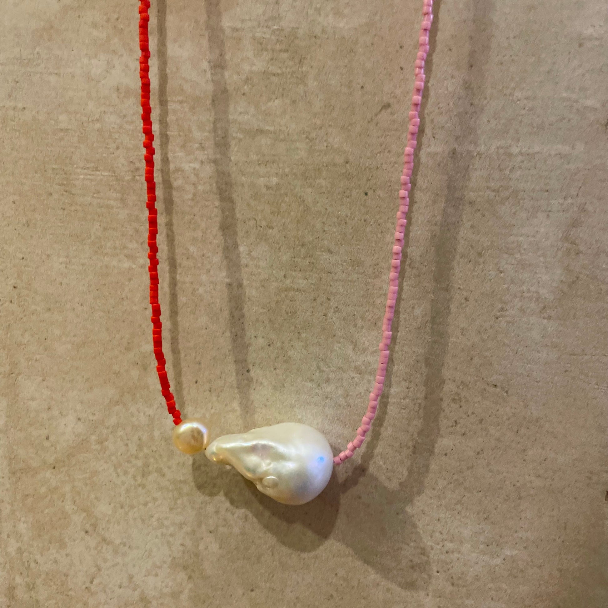 Necklace with two pearls on a red and pink string against a beige background